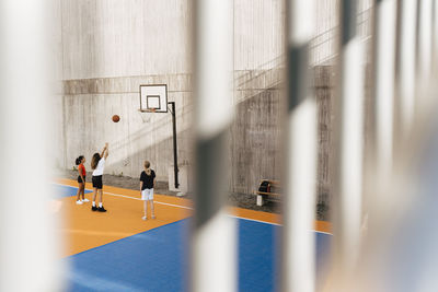 Female friends playing basketball seen through railing at sports court