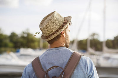 Rear view of man wearing hat and backpack at harbor