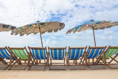 Deck chairs on beach against sky