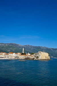 Sea by buildings against blue sky