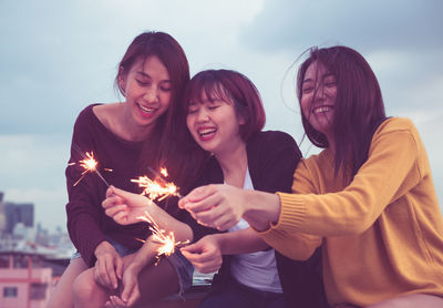 Smiling friends holding sparklers during sunset