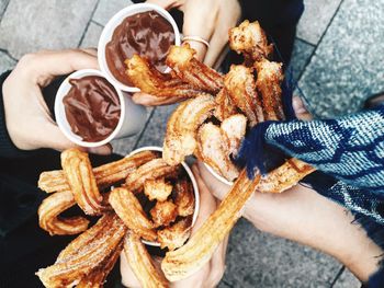 Cropped image of friends holding fresh churros and hot chocolate