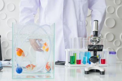 Midsection of scientist standing by fish in tank and microscope at laboratory