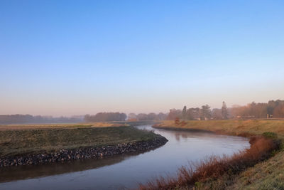 Canal amidst field against clear sky