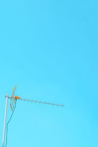 Low angle view of birds perching on cable against clear blue sky