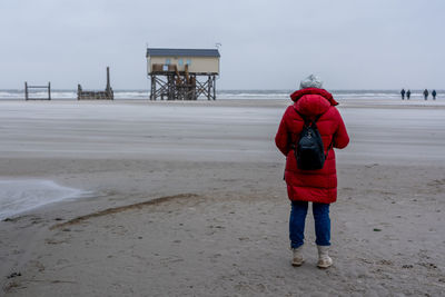 Rear view of woman standing at beach against clear sky