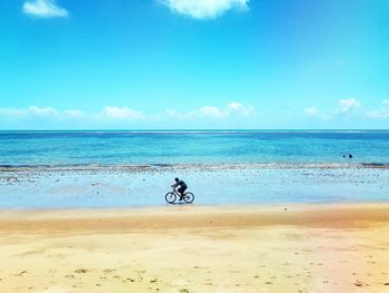 Person riding bicycle on beach against sky