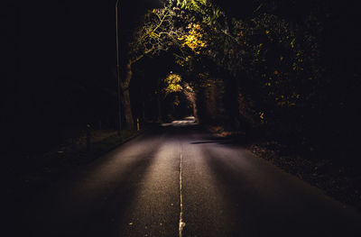 Empty road amidst trees at night