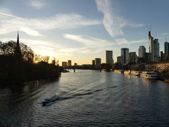 Scenic view of river by buildings against sky during sunset