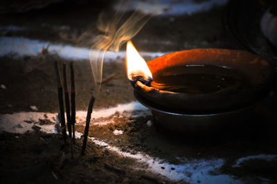 Close-up of lit diya by incense on ground