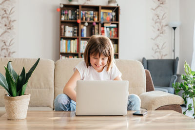 A schoolgirl girl studies at home through a laptop, makes a video call or communicates with friend