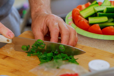 Cropped hands cutting vegetables on cutting board