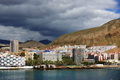 Buildings by sea against cloudy sky