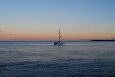 Sailboat sailing on sea against clear sky during sunset