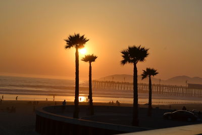 Silhouette palm trees on beach against sky during sunset