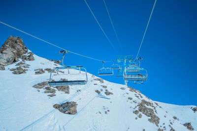 Ski lift over snowcapped mountains against clear blue sky