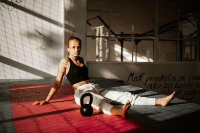 Portrait of young woman sitting by barbell in gym