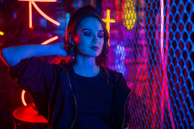 Portrait of young woman standing against illuminated string lights at night