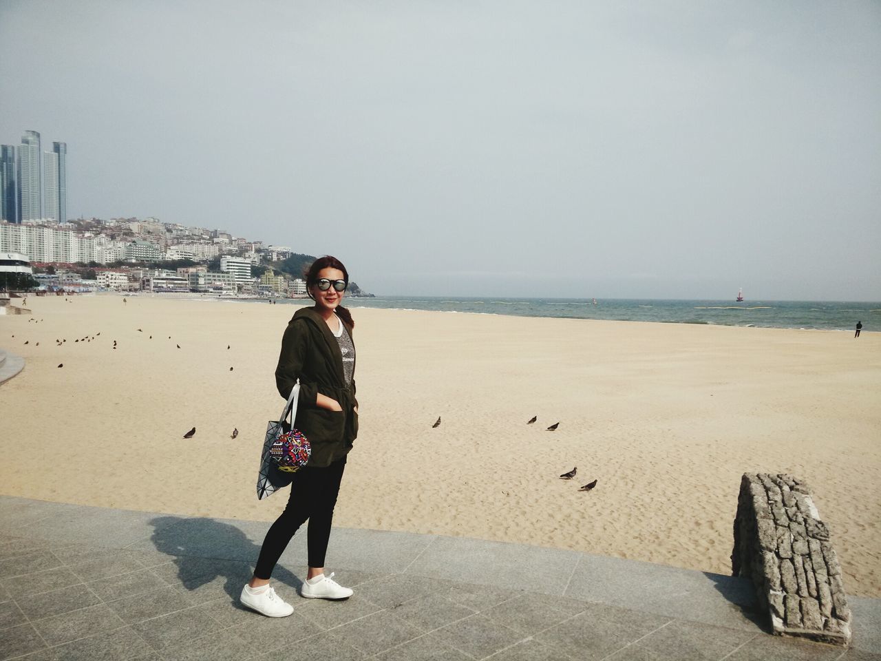 beach, full length, lifestyles, casual clothing, sea, sand, clear sky, leisure activity, shore, young adult, person, water, copy space, built structure, standing, looking at camera, architecture, portrait