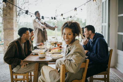 Portrait of happy young woman sitting at dining table with friends during dinner party