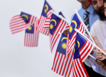Cropped hands holding malaysian flags against white background