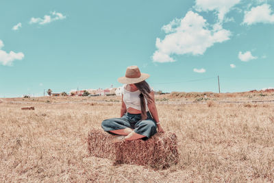 Woman sitting on field against sky