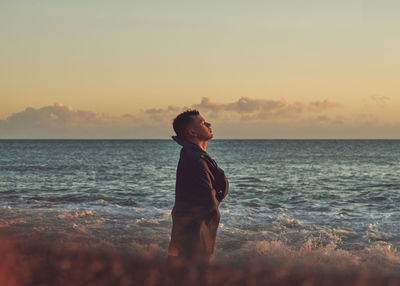 Young man standing at beach during sunset