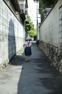 Rear view of woman walking on footpath amidst buildings