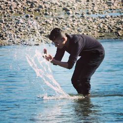 Side view of young man using mobile phone in sea
