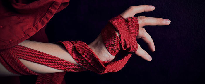 Cropped hands of woman holding red textile against black background