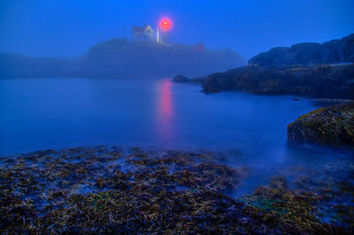 Maine coast lighthouse glows in fog and early morning blue light