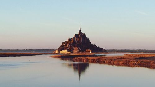 Reflection of mont saint-michel in river against clear sky at dusk