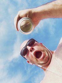 Low angle view of shocked shirtless man holding drink can against sky