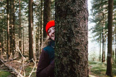 Woman standing by tree trunk in forest