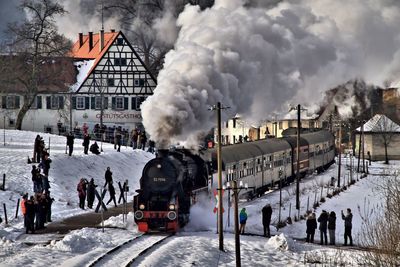 People and a steam-train on snow in city against sky