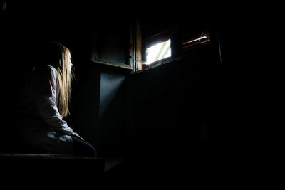 Side view of woman sitting in dark room