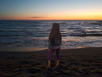 Rear view of girl standing at beach during sunset