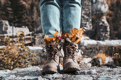 Low section of woman in autumn clothes and fall leaves tucked into her boots.