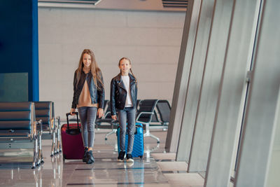 Full length of sisters with luggage walking at airport