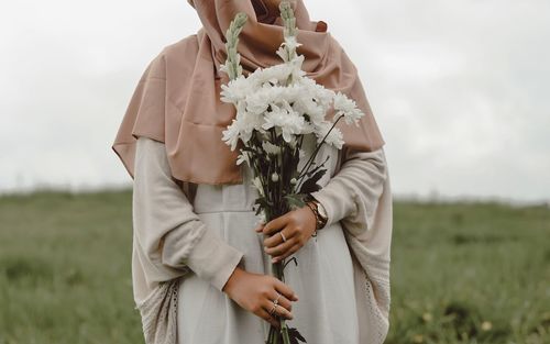 Midsection of woman holding flowers while standing on field