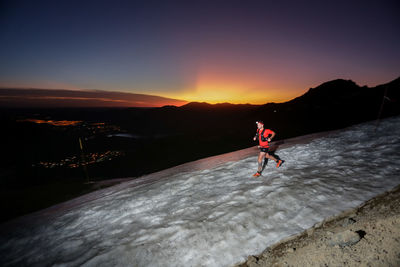 Rear view of man walking on snow covered landscape during sunset