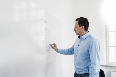 Businessman drawing chart on whiteboard at workplace