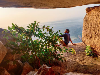 Man sitting on rock by sea against sky