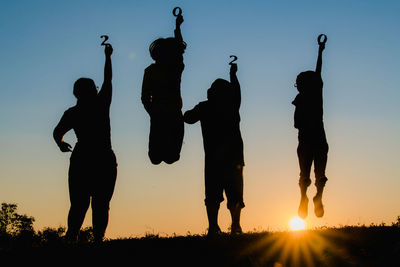 Silhouette people standing on field against sky during sunset