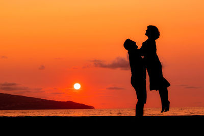 Couple at beach, silhouette in sunset, love and friendship, man lifting woman.