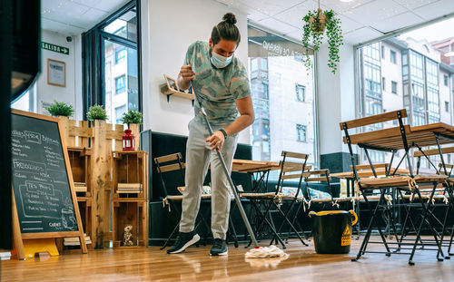 Waiter wearing mask cleaning floor in cafe