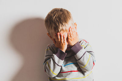 Portrait of boy covering face against white background
