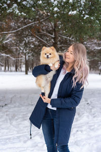 Young woman carrying dog while standing in snow during winter