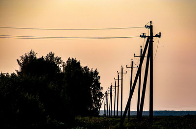 Silhouette electricity pylon on field against sky at sunset