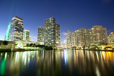 Illuminated buildings by river against sky in city